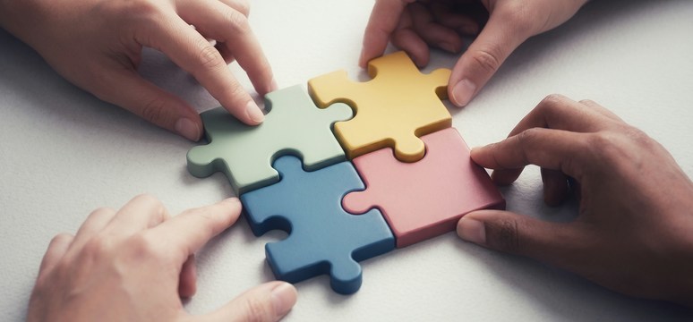 Vier handen maken samen een puzzel.